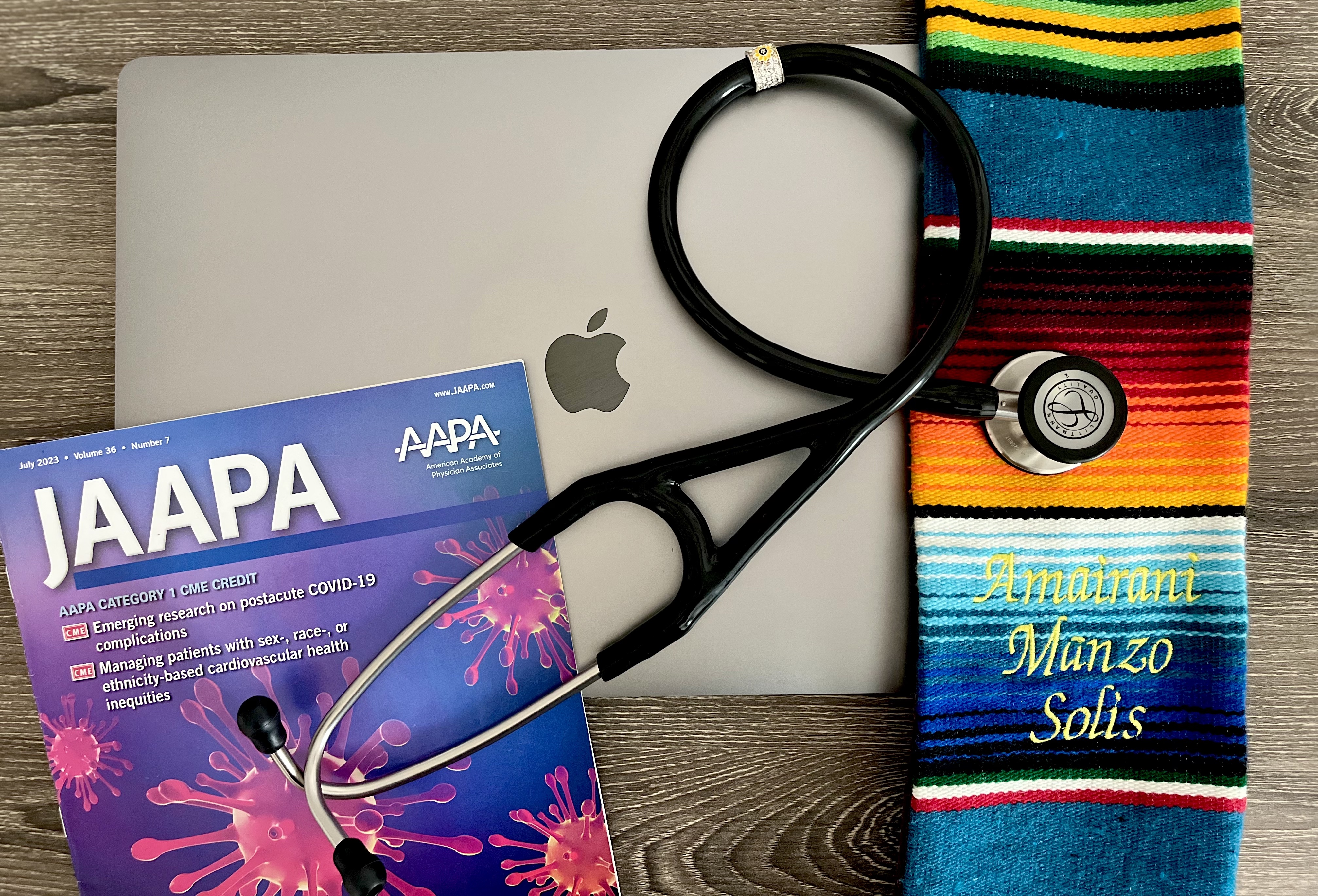 Image of a closed laptop with a stethoscope, JAAPA journal and graduation cords on top