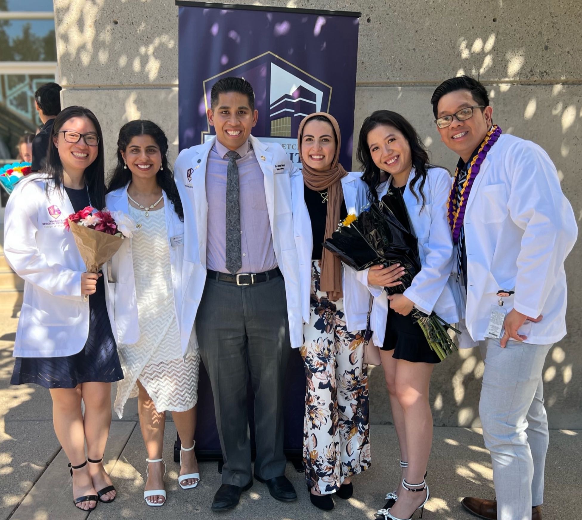 A group of students standing, wearing white coats and some holding flowers